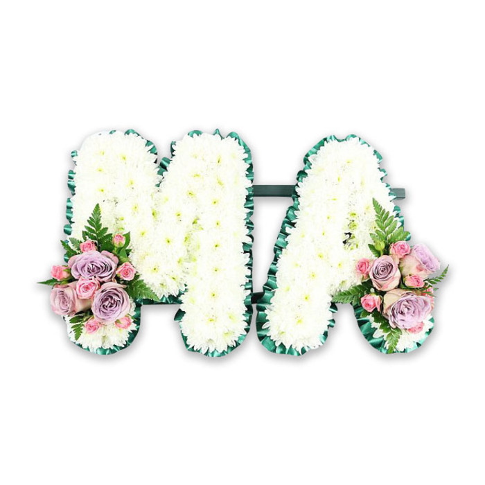 In this image, a bespoke funeral flower tribute spells out the letters MA with quiet grace, photographed against a bright white backdrop that highlights its lines and colours with clarity. The letters themselves are built from a hidden frame, upon which a thick layer of white chrysanthemums has been carefully arranged. Each bloom is fresh and round, with multiple delicate petals radiating from a soft centre, and they are placed so closely that the surface appears continuous and cushiony, like a blanket of petals. The overall tone of the flowers drifts between bright white and creamy ivory, giving the arrangement a natural, gentle variation under the light. Along the outer edge of each letter, a deep emerald green border provides a strong contour, probably created with pleated ribbon or closely set foliage. This border adds clean definition to every angle and curve, ensuring the M and the A read clearly from across a room, much as a name on a memorial board might stand out in a Somers Town church or community hall. The two letters are anchored together by a slim dark green bar at the base, discreet but effective in keeping them aligned. At the lower left base of the M and lower right base of the A, two subtle yet striking accent sprays are positioned. These small bouquets combine lilac roses, pale pink roses, and clusters of pink spray roses, with each petal forming soft spirals of colour from delicate blush to dusky lavender. Slender fern fronds extend from the sides, accompanied by touches of fresh greenery, giving a light, feathery movement that hints at a walk through nearby St Pancras Churchyard. This MA tribute feels deeply personal, often commissioned for a mother, Mama, or someone with those initials, and would make a thoughtful focal piece at a funeral, memorial service, or graveside gathering for families in and around Somers Town.