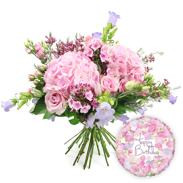 A softly lit, celebratory composition features a hand-tied bouquet and birthday balloon set against a pure white background, creating a clean stage where the colours and textures of the flowers recall the gentle charm of residential streets around Somers Town. The bouquet is rich and rounded, built around several large clusters of blush pink hydrangea whose dense, tightly packed petals form velvety mounds. These hydrangea heads, each made up of many tiny florets, lend the arrangement a sense of fullness and romance. Intertwined with them are light pink roses, some just beginning to open, others more fully expanded to reveal their beautifully layered centres. Their petals curl elegantly, giving the impression of soft movement and adding a classic, timeless note. Smaller accents of deeper pink or fuchsia waxflowers are carefully tucked between the larger blooms, creating lively pockets of colour and intricate texture, like miniature fireworks against the softer pastels. Graceful stems of campanula rise slightly above and through the bouquet, their bell-shaped flowers in shades of lavender and periwinkle providing cool, airy highlights that balance the pink tones. Surrounding and supporting the blooms is an assortment of fresh green foliage, from slim, pointed leaves to more substantial, glossy greens that add depth and frame the design. The stems at the base are gathered together neatly, characteristic of a professional hand-tied bouquet ready for a vase on a birthday table near Eversholt Street or beside a cosy reading chair. To the lower right of the floral display, a round Mylar Happy Birthday balloon adds a playful shimmer. Its surface is adorned with a repeating pattern of tiny roses and buds in coordinating pinks, lilacs, and creams, while in the centre, flowing script in rich purple clearly spells out Happy Birthday, linking the entire arrangement to the occasion it celebrates.