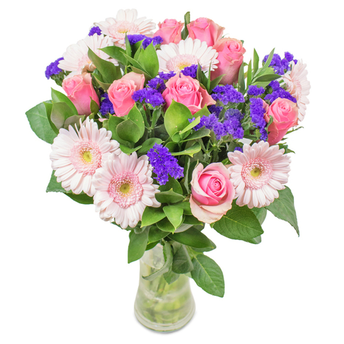 Set against a crisp white background, this dynamic Somers Town bouquet is an ode to local botanical artistry. The core is composed of roughly seven to nine soft-to-medium pink roses, their petals elegantly swirling-some still tightly furled, others unfolding to reveal the classic rose shape familiar from the flower markets of Chalton Street. These blooms are beautifully paired with five to seven pale pink Gerbera daisies, each boasting a large round face with pale-to-white centers, infusing the arrangement with a gentle, luminous quality reminiscent of the morning sun filtering into St. Pancras Gardens. Clusters of vivid purple statice or limonium are interspersed throughout, providing an energizing pop of colour and tactile contrast that calls to mind the creative vibrancy of the local art scene. A generous base of deep green, glossy foliage elevates the sense of freshness and brings the abundance of the nearby parks into focus. All elements are gathered in a transparent vase that completes the natural look, displaying both the stems and the purity of clean water. Perfect for birthdays, anniversaries, Mother's Day, or simply as a thoughtful gift delivered within Somers Town, this arrangement conveys joy, celebration, and heartfelt affection with every petal.
